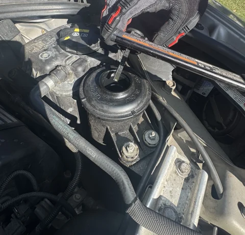 A gloved hand holding a dipstick above an open fluid reservoir.